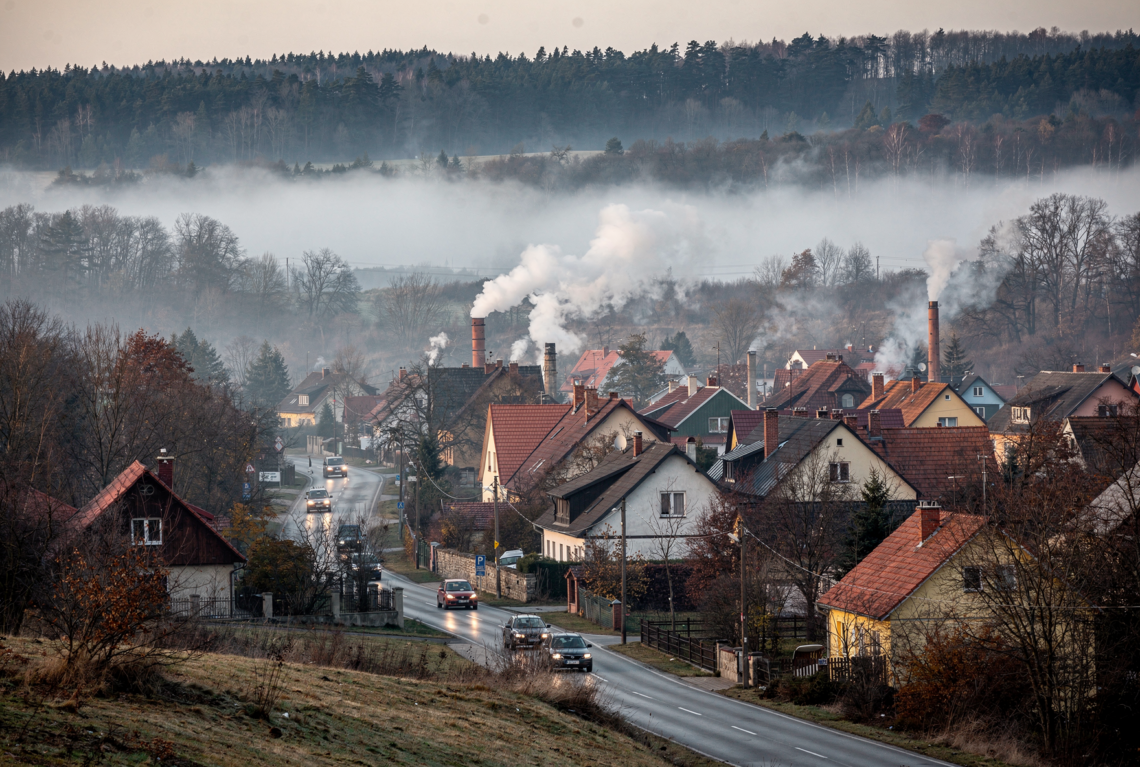 vesnice v údolí, kde kouří hodně komínů a je tu smog, v okolí na kopcích je les, kopce jsou nízké, v údolí také jede několik aut po silnici