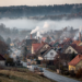 vesnice v údolí, kde kouří hodně komínů a je tu smog, v okolí na kopcích je les, kopce jsou nízké, v údolí také jede několik aut po silnici